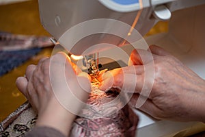 A close-up view of sewing process, hand of old woman using sewing machine, selective focus technique