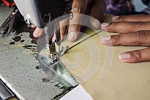 Close up view of sewing process. Hands stitching fabric on professional manufacturing machine at workplace