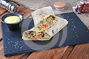 Close up view on Shawarma sandwich, gyro fresh roll in lavash. Shaurma served on black stone. Kebab in pita with copy space.