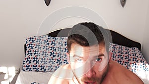 Close up view of shocked young caucasian man oversleep and getting up fast while lying in bed . Handsome man waking up