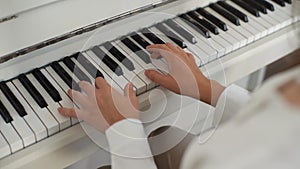 Close-up view from shoulder of unrecognizable female pianist playing on classical piano at home enjoying virtuoso music