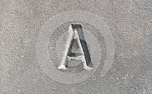 Close-up view of a single one letter A carved into a smooth gray stone. Latin alphabet letters, written language history, culture
