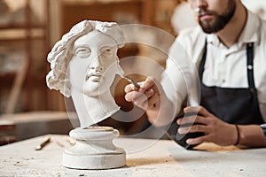 Skillful sculptor makes professional restauration of gypsum sculpture of woman`s head at the creative workshop. photo