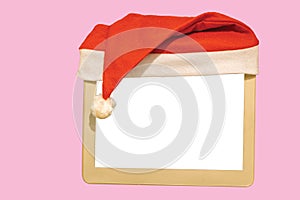 Close up view of small white mockup image blank board with red Santa hat over top isolated on pink background.