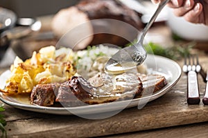 A close-up view of a spoon with sauce that pours over the meat, roasted neck. As a side dish to the meat are baked potatoes and