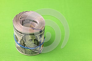 Close up view of stack of 100 dollar bills rolled into roll isolated on green background.