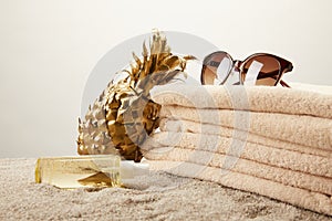 close up view of stack of towels, sunglasses, tanning oil and golden decorative pineapple on sand on grey backdrop