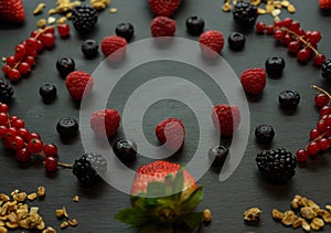 Close up view of strawberries, blackberries, blueberries, raspberries, currants and granola on a black slate background. Healthy