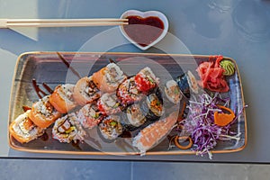 Close-up view of a sushi platter with various sushi, sauce, and wooden chopsticks on the table in a restaurant.