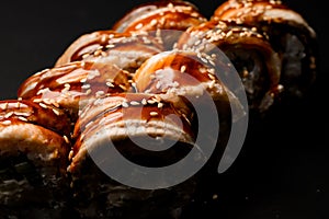 Close-up view of sushi rolls Philadelphia with smoked eel with soy sauce and sesame seeds on dark background.