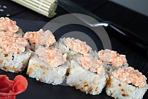 Close up view on sushi rolls with with red fish, okra and Philadelphia cheese on a black coal board and a wooden background.