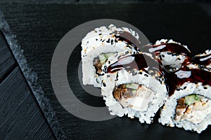 Close up view on sushi rolls with with red fish, okra and Philadelphia cheese on a black coal board and a wooden background.