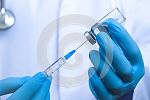 Close up view on syringe and glass ampoule in hands dressed in blue rubber gloves, white robe dressed doctor