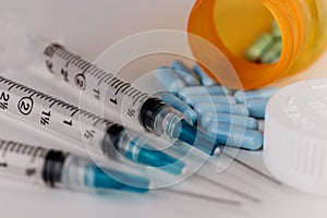 Close up view of a syringe with hypodermic needle and generic blue pills. Opiate and heroin overdoses have skyrocketed VII