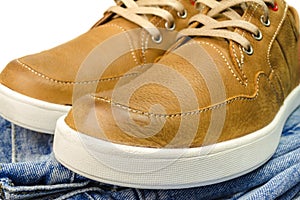 Close-up view of tan color, leather sneakers on jeans pant.