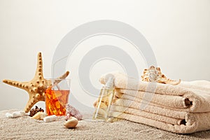 close up view of tanning oil, refreshing cocktail with ice, towels, sea star and seashells on sand on grey background