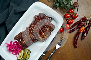 Close up view on tasty delicious bbq coocked ribs with barbecue sauce in white plate on wooden background. Classical american