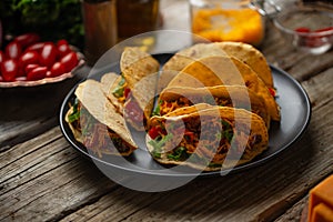 Close-up view of tasty mexican tacos on black round plate on rustic wooden table. Traditional mexican cuisine. Ingredients for