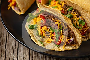 Close-up view of tasty mexican tacos with meat on black round plate on rustic wooden table. Traditional mexican cuisine