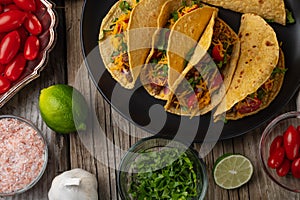 Close-up view of tasty street tacos with beef, tomatoes, onion and cheese on black round plate. Ingredients for cooking tacos on