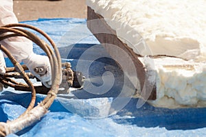 Close up view of technician dressed in a protective white uniform spraying foam insulation using Plural Component Spray Gun.