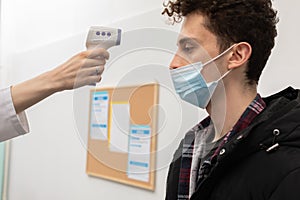 Close-up view. Temperature measurement of a young man in the entrance of a clinic, performed by medical staff in the