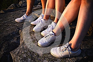 Close up view of three pairs of legs in white sneakers in nature at sunset