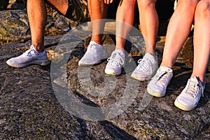 Close up view of three pairs of legs in white sneakers in nature at sunset