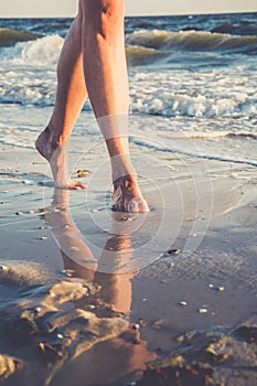 Close up view to female feet. Reflection in the water, barefoot young woman walking on the sand beach