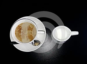 A close-up view of the top and side cups of coffee and a saucer and a jug with milk.