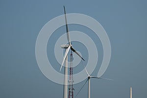 Close up view of the top of two wind turbines against a clear blue sky