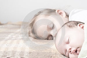 Close up view of two children, newborn baby,three year old girl sleeping together on beige bed. Sisters are sleeping on