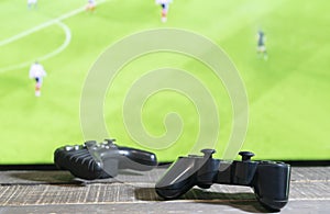 Close up view of two game pad video console controller with soccer match, green screen television on background.Gaming concept