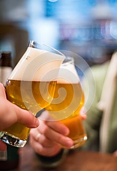 Two glass of beer in hand. Beer glasses clinking in bar or pub