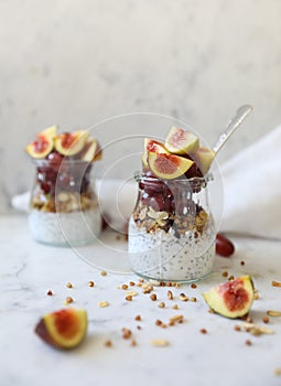 Close up view of two glasses filled with yogurt with chia seeds, granola, fresh figs and purple grapes drizzled with honey against