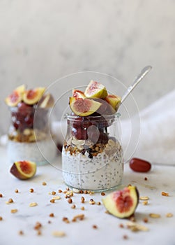 Close up view of two glasses filled with yogurt with chia seeds, granola, fresh figs and purple grapes drizzled with honey against