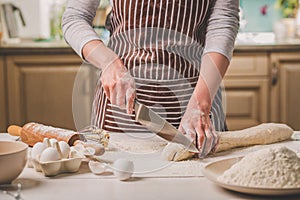 Close-up view of two woman`s hands cut knife dough