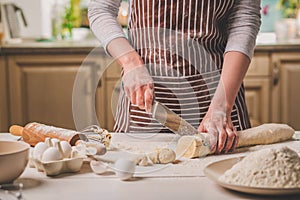 Close-up view of two woman`s hands cut knife dough