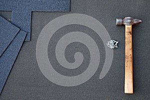 Close up view on unfinished asphalt roofing shingles background with hammer and nails