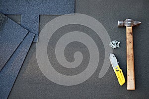 Close up view on unfinished asphalt roofing shingles background with hammer and nails. Installation of waterproofing coating in co