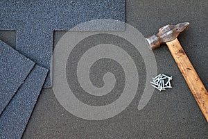 Close up view on unfinished asphalt roofing shingles background with hammer and nails. Installation of waterproofing coating in co