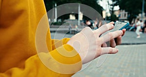 Close-up view of the unknown male hands in yellow sweater texting and browsing on the mobile phone outdoor. 4k footage.