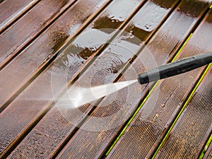 Close up view of using pressure washer to clean impregnated wood terrace outdoors in the spring.