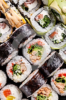 Close-up view of various sushi rolls with different fillings on black metal slate.