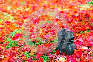 Close-up view of a Warabe Jizou stone carving with the image of an adorable child on the ground covered with fallen leaves