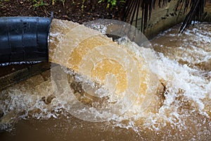 A close-up view of water violently flowing from a steel pipe near the concrete shore