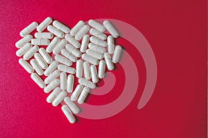 Close up view of white capsules forming a heart on red background with space