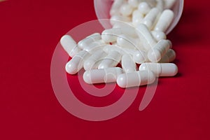 Close up view of white capsules spilling from a bottle on red background with space