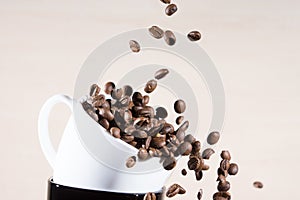 Close up view of white cup standing on black cup with falling down brown roasted coffee beans.