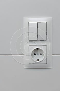 Close up view of white light swithch and socket pair on white tile. Building construction elements concept. Interior. Design